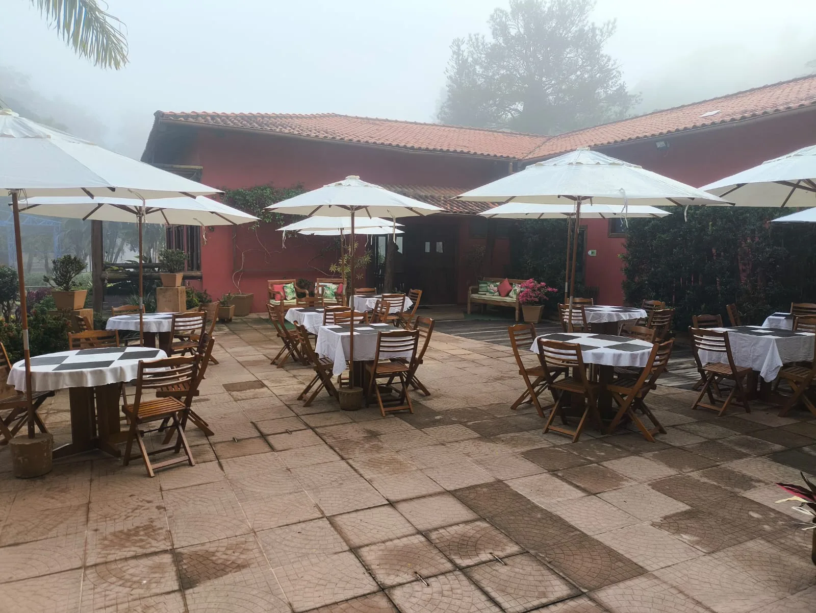 Varanda com mesas e guarda-sóis em manhã de neblina